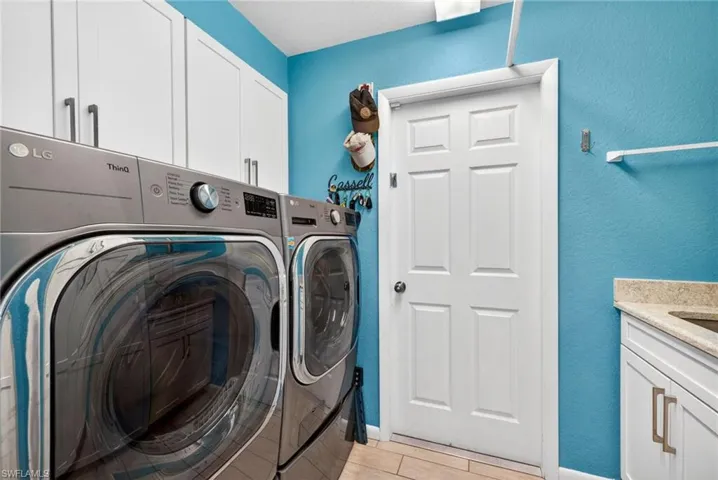 Laundry area featuring white cabinetry, a six-panel interior door, a built-in countertop with an undermount sink, and tile flooring