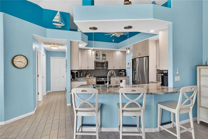 Kitchen featuring a breakfast bar with stone-look countertop, stainless steel appliances, and light-toned cabinetry