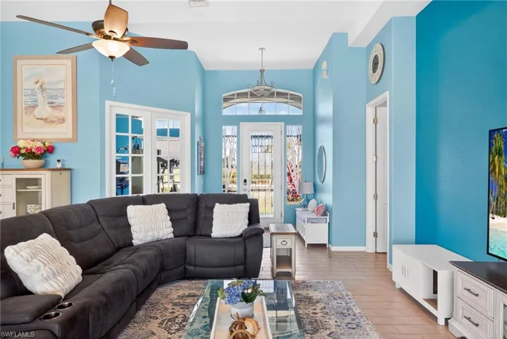 Vaulted ceilings, wood-finish flooring, ceiling fan with integrated lighting, glass-paneled French doors, and transom window