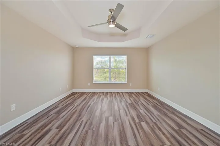 Spacious room featuring wood-finish flooring, a tray ceiling, and a modern ceiling fan with integrated lighting