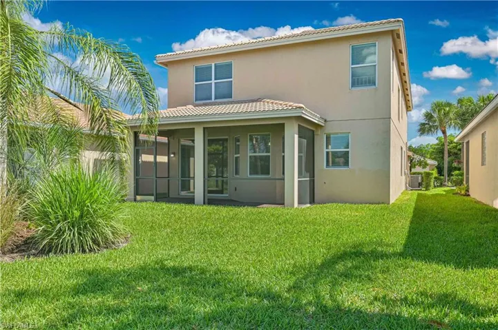 Expansive green lawn with a screened patio, two-story stucco exterior, and tile roof