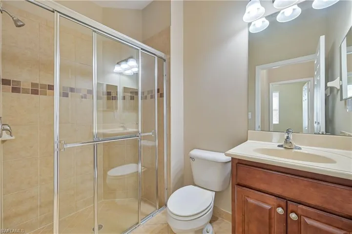Shower enclosure with sliding glass doors, tan ceramic tile surround, and decorative accent tiles