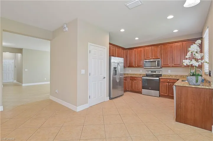 Spacious kitchen featuring warm-toned cabinetry, stainless steel appliances, speckled stone countertops, and recessed lighting