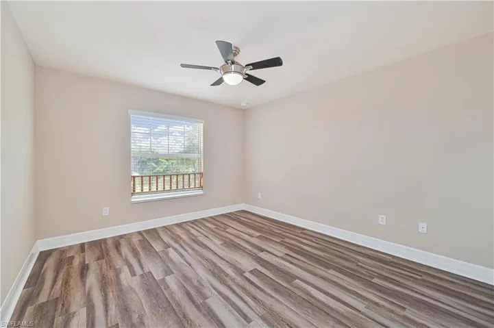 Room with wood-finish flooring, a contemporary ceiling fan with integrated lighting, and a single window with horizontal blinds and a decorative railing