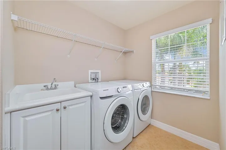 Laundry room featuring a window with white blinds, a utility sink with white cabinetry, and a wire shelving unit