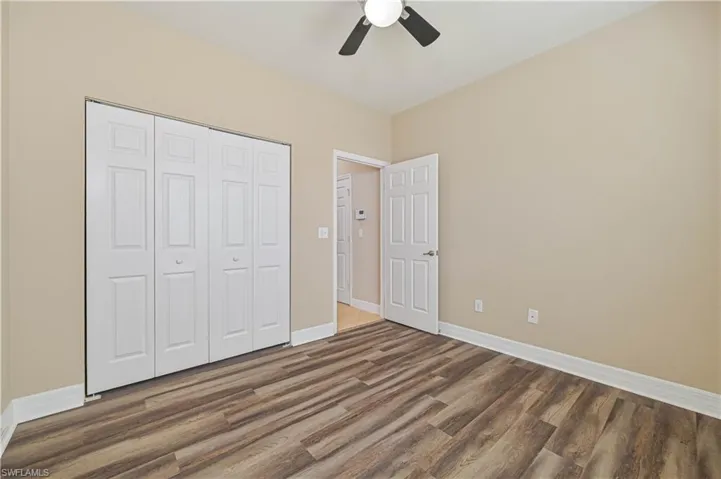 Light-toned walls complement wood-finish flooring in this room featuring a ceiling fan, white bi-fold closet doors, and white baseboards
