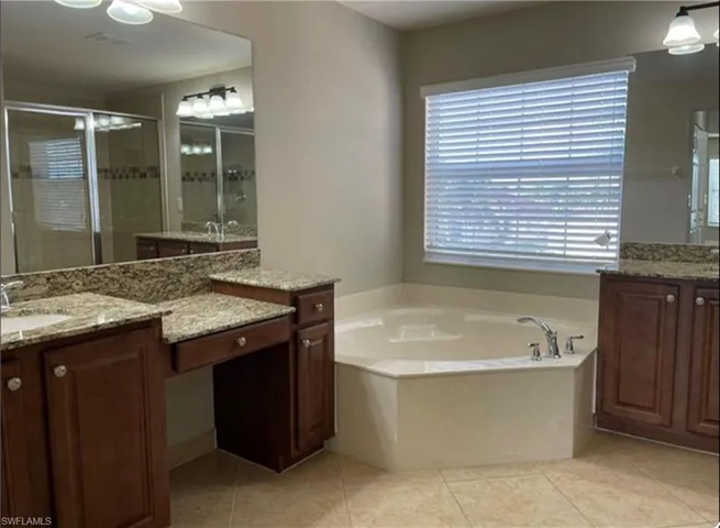 Bathroom featuring two vanities, a stall shower, light tile patterned flooring, and a bath