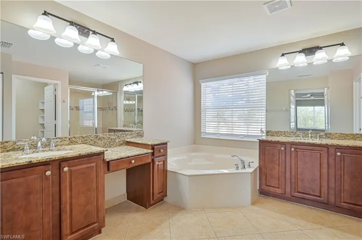 Dual wood-finish vanities with granite countertops, integrated sinks, and individual wall-mounted light fixtures