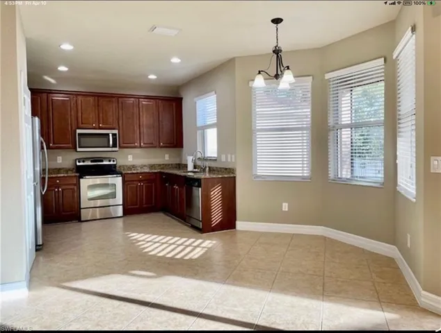 Kitchen featuring stainless steel appliances, hanging lights, light tile patterned floors, and light stone countertops