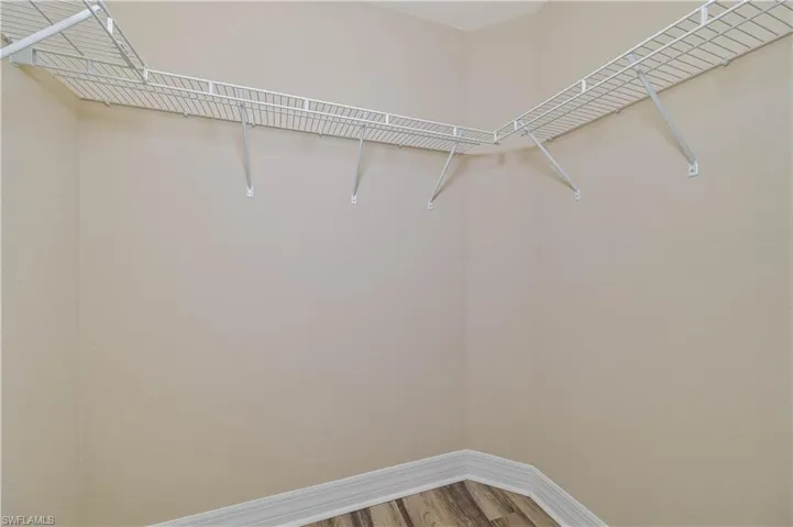 Corner storage area featuring L-shaped wire shelving, baseboard trim, and wood-finish flooring