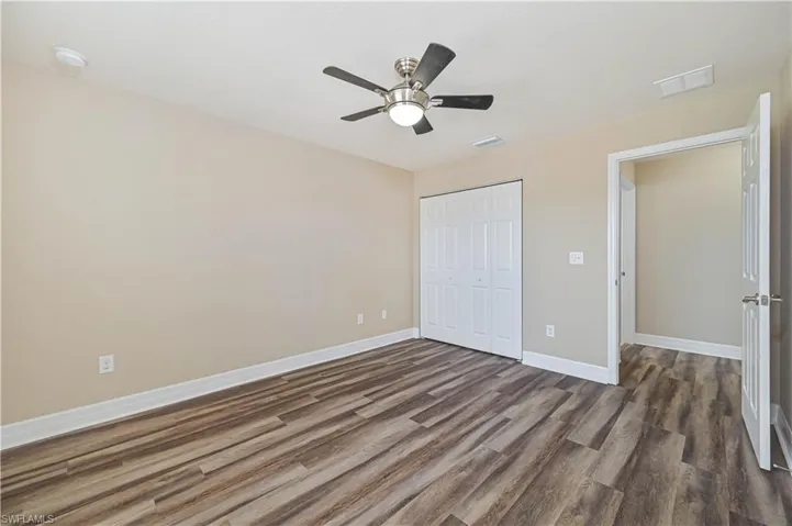 Room featuring wood-finish flooring, neutral wall tones, bi-fold closet doors, a ceiling fan with integrated lighting, and white baseboards