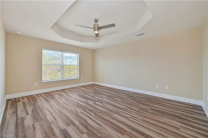 Spacious room featuring wood-finish flooring, a tray ceiling with a contemporary ceiling fan, and a large window with horizontal blinds