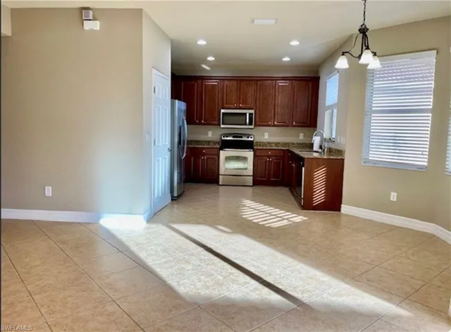 Kitchen with stainless steel appliances, hanging lights, light stone countertops, and light tile patterned floors