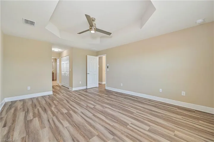 Spacious interior room featuring wood-finish flooring, a contemporary ceiling fan, and a tray ceiling