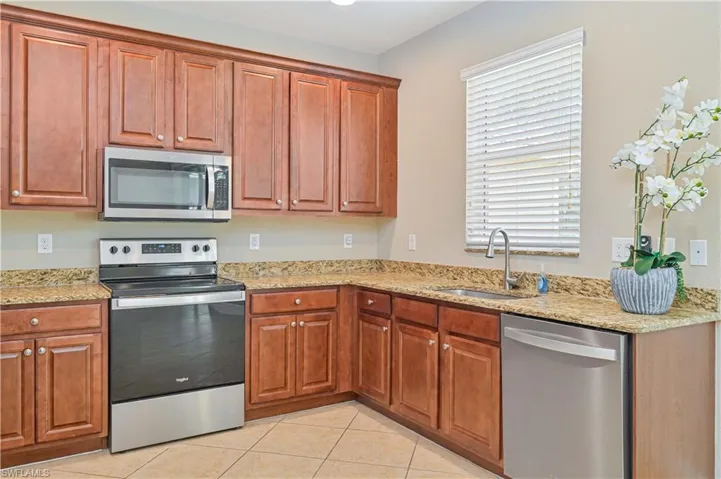 Kitchen featuring wood-finish cabinetry, granite countertops, stainless steel appliances, and tile flooring
