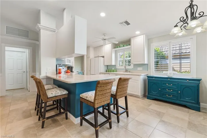 Kitchen featuring a peninsula, a kitchen breakfast bar, white cabinets, hanging light fixtures, and a ceiling fan