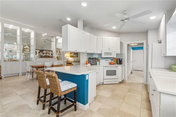 Kitchen featuring a ceiling fan, white cabinets, white appliances, a breakfast bar area, and recessed lighting