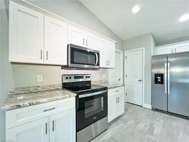 Kitchen with appliances with stainless steel finishes, vaulted ceiling, light wood-type flooring, light stone countertops, and white cabinetry
