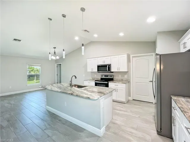Kitchen featuring lofted ceiling, white cabinets, stainless steel appliances, sink, and a center island with sink