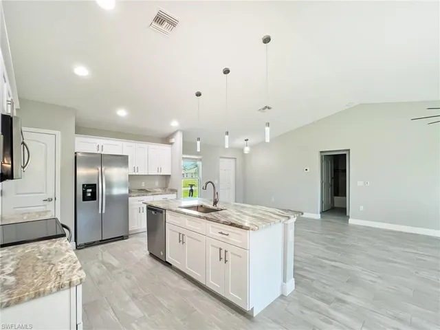 Kitchen with white cabinets, stainless steel appliances, light stone countertops, sink, and a center island with sink
