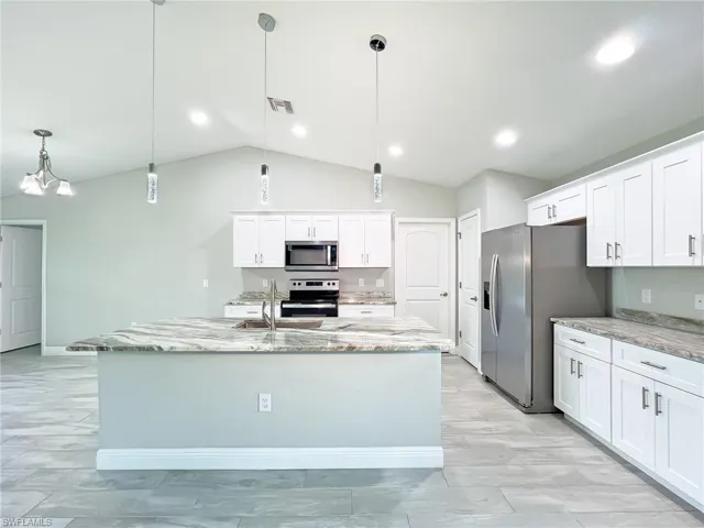 Kitchen featuring white cabinets, light stone counters, appliances with stainless steel finishes, pendant lighting, and vaulted ceiling
