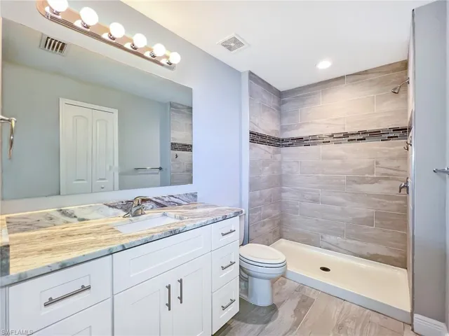 Bathroom with tiled shower, hardwood / wood-style flooring, toilet, and vanity
