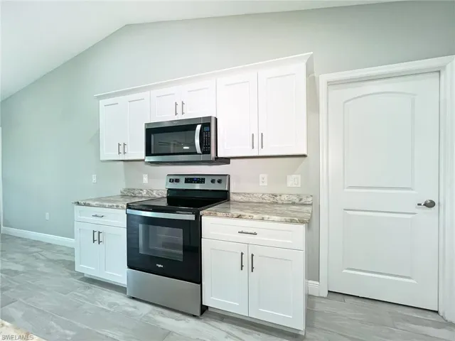 Kitchen with appliances with stainless steel finishes, lofted ceiling, white cabinets, and light stone countertops