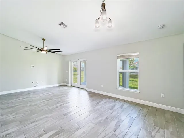 Empty room with ceiling fan with notable chandelier, light hardwood / wood-style floors, and a wealth of natural light