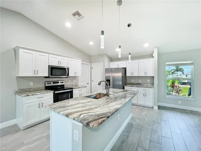 Kitchen with white cabinets, pendant lighting, sink, appliances with stainless steel finishes, and lofted ceiling