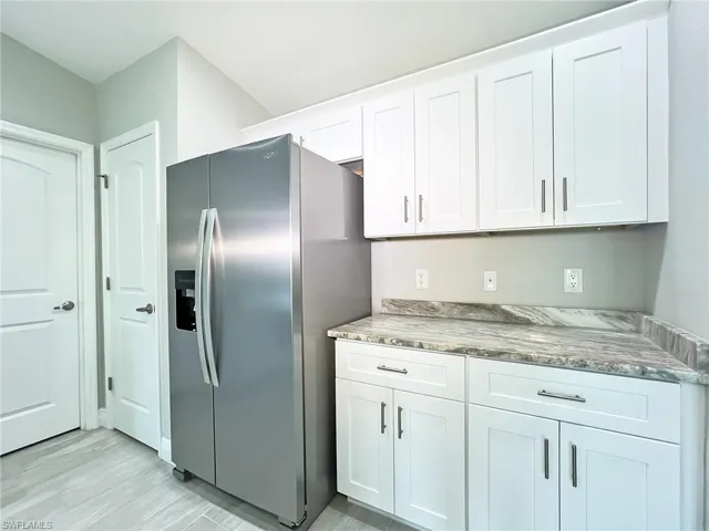 Kitchen with white cabinetry, light stone countertops, and stainless steel fridge