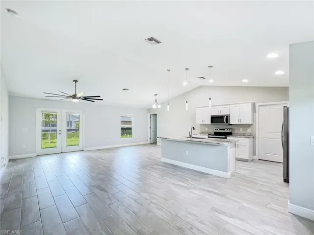 Kitchen with appliances with stainless steel finishes, vaulted ceiling, a center island with sink, sink, and white cabinetry
