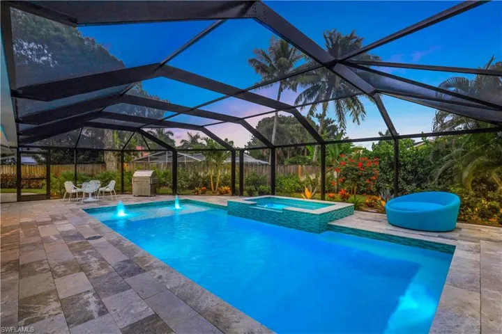 Pool at dusk with an in ground hot tub, glass enclosure, a patio area, and pool water feature