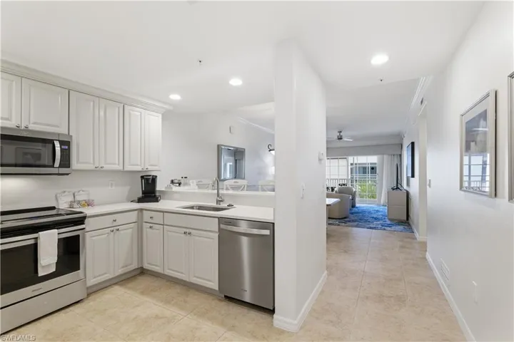 Kitchen with appliances with stainless steel finishes, open floor plan, light tile patterned floors, crown molding, and white cabinetry