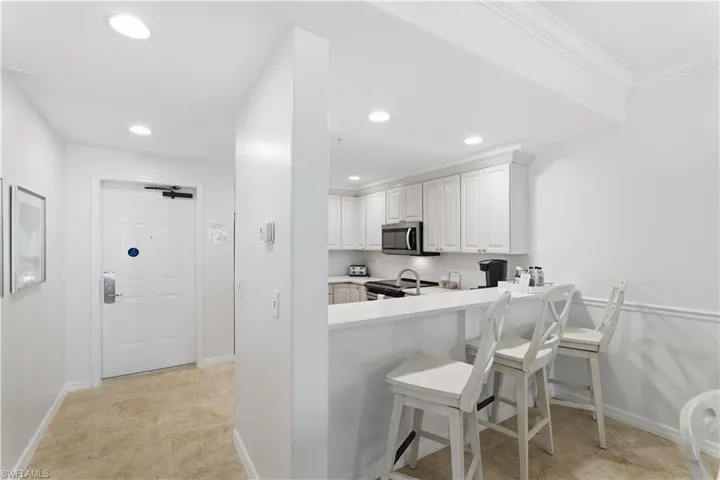 Kitchen with light countertops, light tile patterned flooring, a breakfast bar, stainless steel microwave, and white cabinets