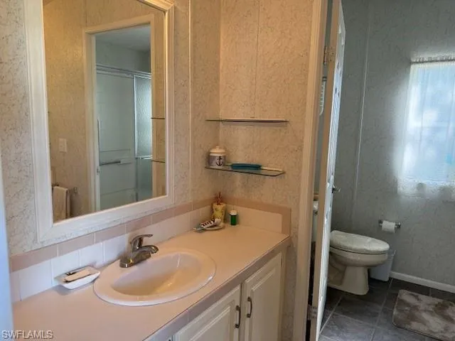 Bathroom featuring tile patterned floors, toilet, an enclosed shower, and vanity