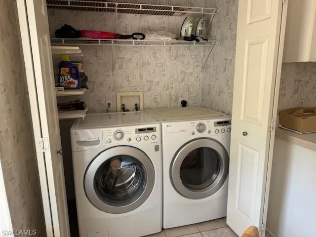 Clothes washing area with light tile patterned floors and washer and clothes dryer