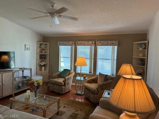 Living room featuring ceiling fan, crown molding, a textured ceiling, and hardwood / wood-style flooring