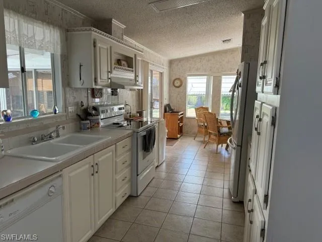 Kitchen featuring dishwashing machine, stove, a textured ceiling, and white cabinetry