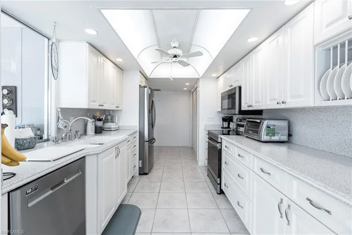 Kitchen with white cabinetry, light tile patterned flooring, ceiling fan, stainless steel appliances, and backsplash