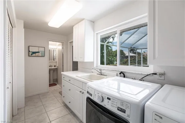 Laundry area featuring light tile patterned flooring, independent washer and dryer, cabinets, and sink