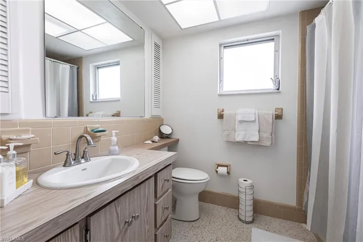 Bathroom featuring backsplash, toilet, vanity, and tile walls