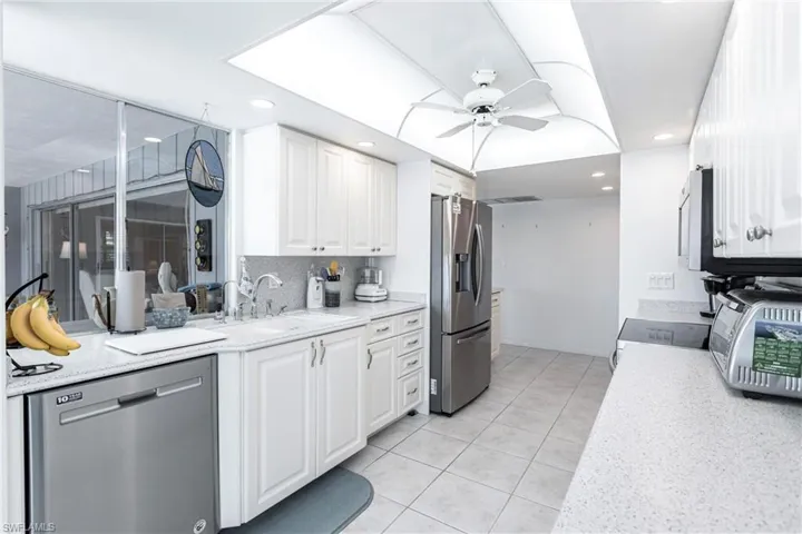 Kitchen featuring white cabinets, light stone counters, ceiling fan, appliances with stainless steel finishes, and sink
