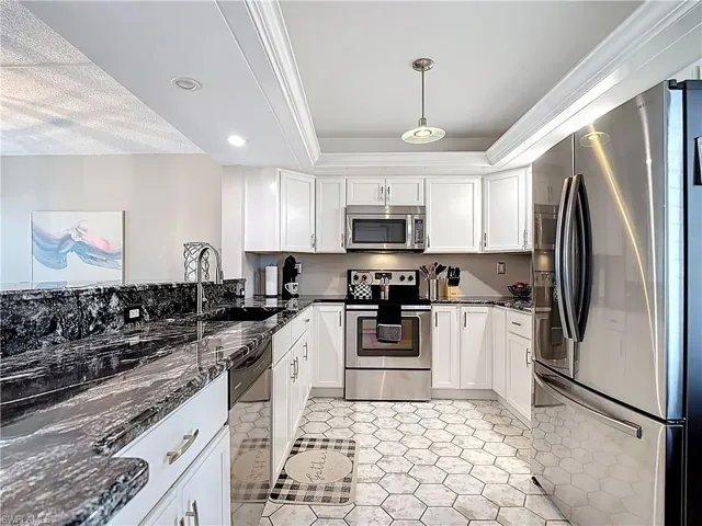 Kitchen featuring stainless steel appliances, white cabinetry, dark stone counters, recessed lighting, and crown molding