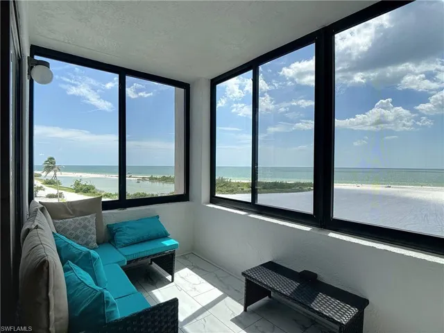 Sunroom with marble look tile flooring, view of water and beach, a textured ceiling, and healthy amount of natural light