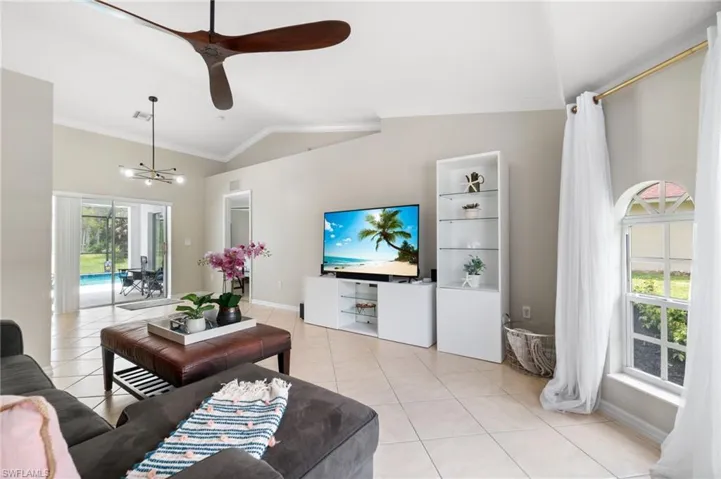 Tiled living room with ceiling fan with notable chandelier, lofted ceiling, and crown molding