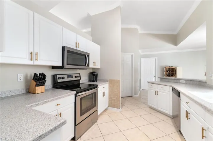 Kitchen featuring white cabinets, a high ceiling, light tile flooring, crown molding throughout, and stainless steel appliances