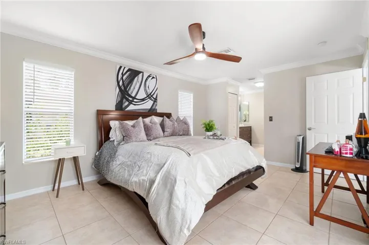 Tiled bedroom with crown molding, ceiling fan, and ensuite bathroom