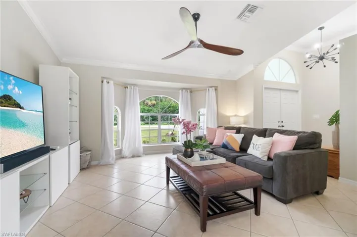 Tiled living room featuring ceiling fan with notable chandelier and ornamental molding