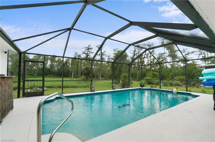View of swimming pool featuring glass enclosure, a patio area, and a yard
