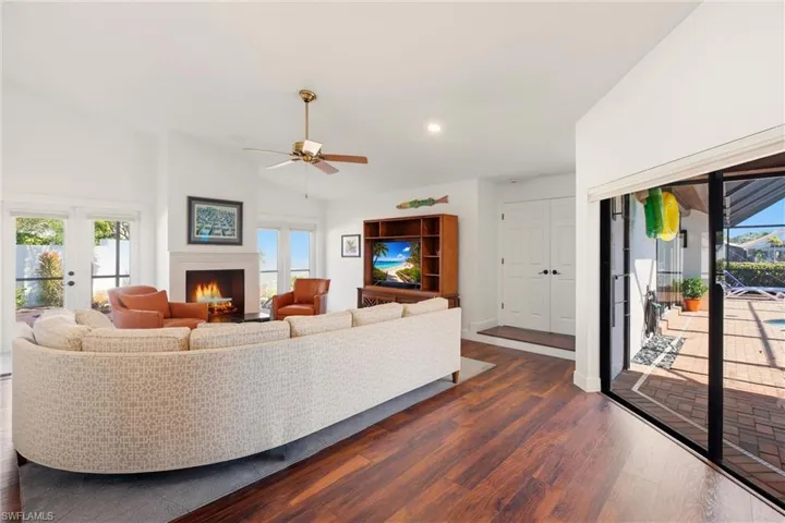 Living area featuring lofted ceiling, dark wood finished floors, ceiling fan, a warm lit fireplace, and french doors
